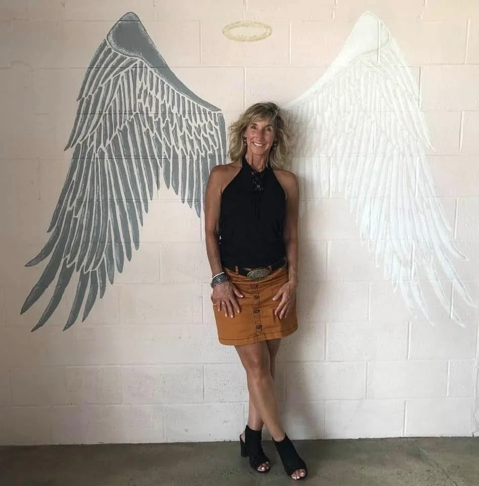 Theresa smiling in front of a wall mural of angel wings and a golden halo